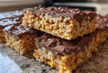 Close-up of stacked peanut butter rice krispie treats topped with a thick layer of melted chocolate.