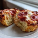 Two halves of a baked pepperoni pizza muffin showing the fluffy interior and cheesy, browned top.