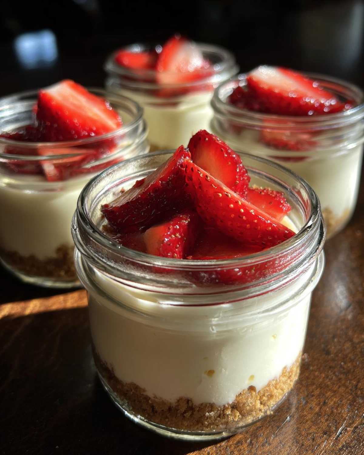 Four individual servings of Protein Cheesecake in small glass jars topped with fresh sliced strawberries.