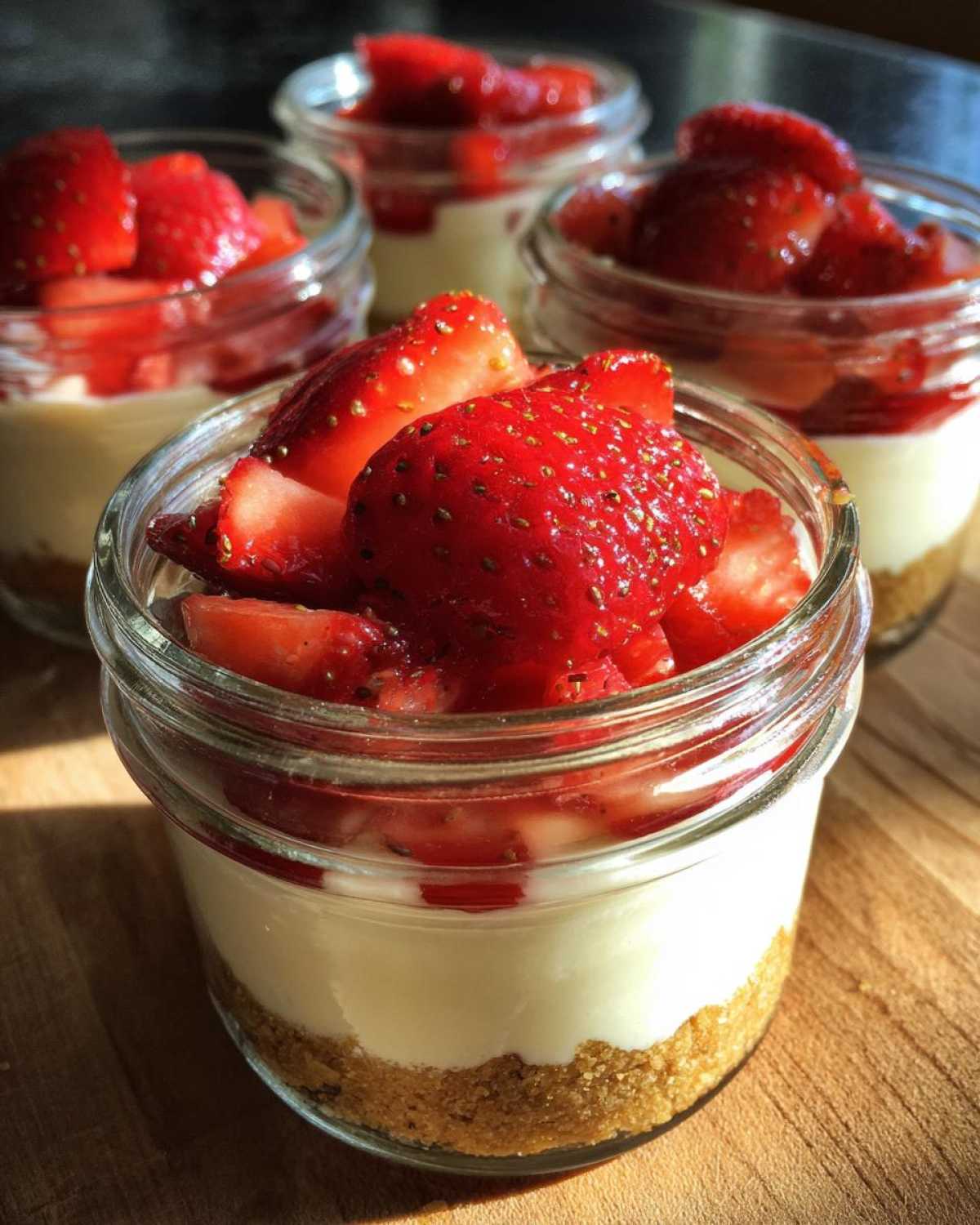 Close-up of a single serving Protein Cheesecake in a jar layered with graham cracker crust and topped with fresh strawberries.