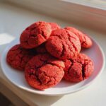 A small pile of vibrant red velvet cake mix cookies with cracked tops sitting on a white plate.