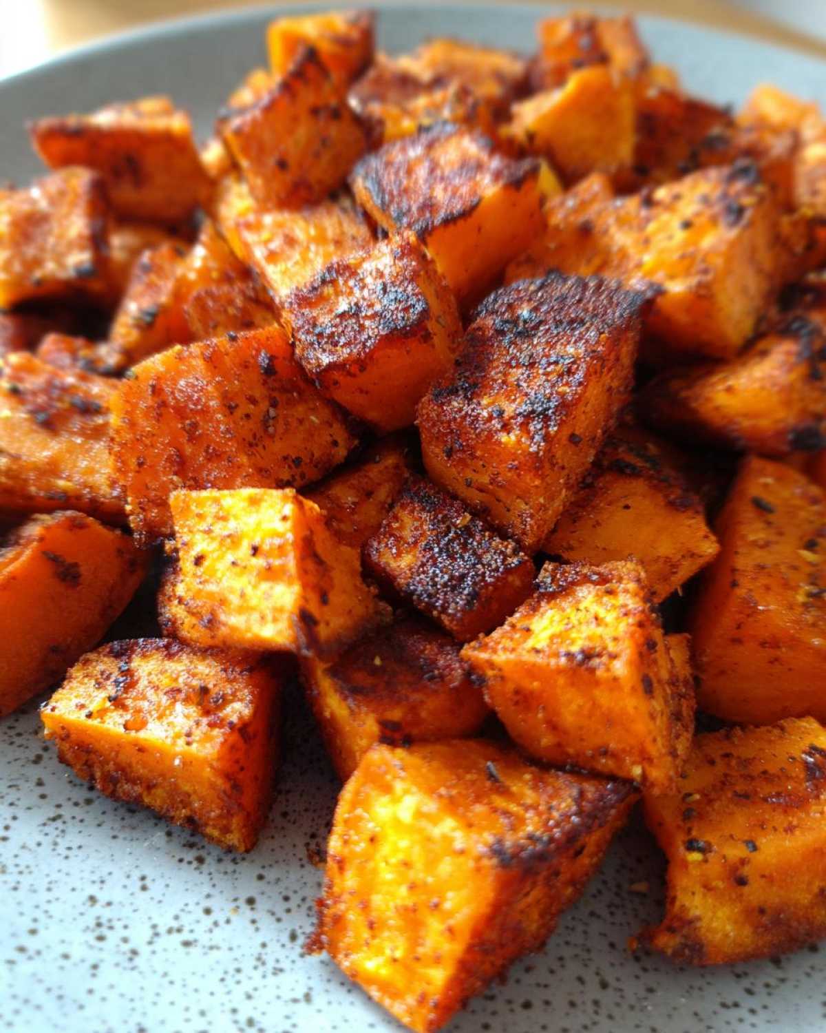 Close-up of perfectly seasoned and caramelized roasted sweet potato cubes piled on a speckled gray plate.