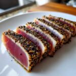 Five slices of perfectly cooked Seared Ahi Tuna, crusted with black and white sesame seeds, showing a rare pink center.