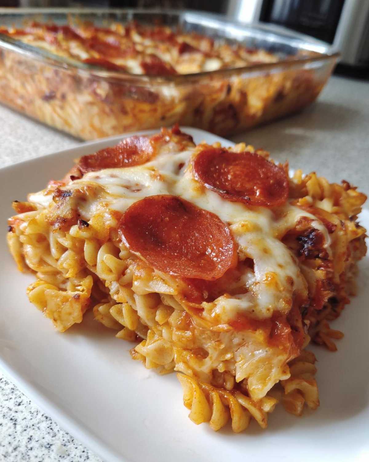 A close-up serving of baked pizza pasta topped with melted cheese and pepperoni slices.