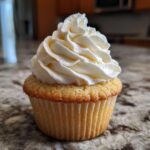 A single, perfectly baked vanilla cupcake topped with a swirl of white buttercream frosting.