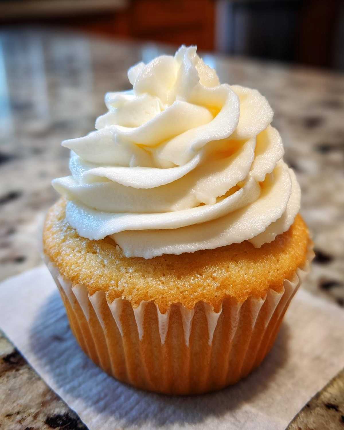 A close-up of a single, perfectly baked vanilla cupcakes topped with a swirl of creamy white frosting.
