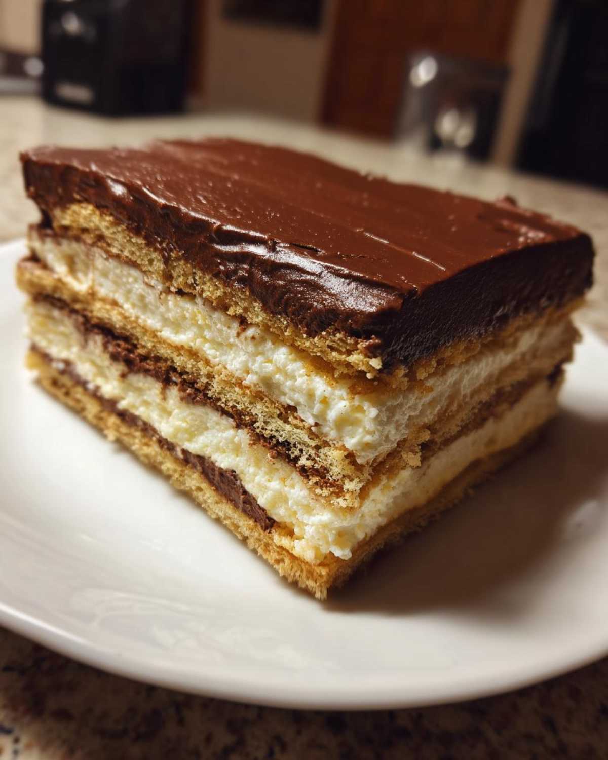 A thick slice of layered eclair cake with graham crackers, vanilla cream, and chocolate frosting.