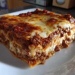 A thick, layered slice of homemade lasagna featuring rich meat sauce and melted, browned cheese on top.