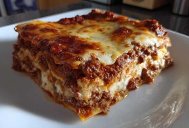 A thick, layered slice of homemade lasagna featuring rich meat sauce and melted, browned cheese on top.