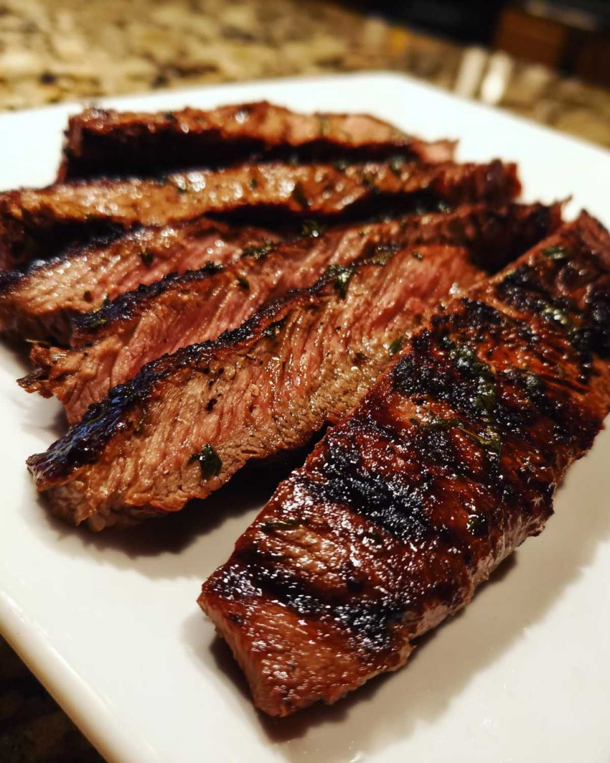 Close-up of medium-rare sliced steak showing grill marks, seasoned with herbs from the carne asada marinade.