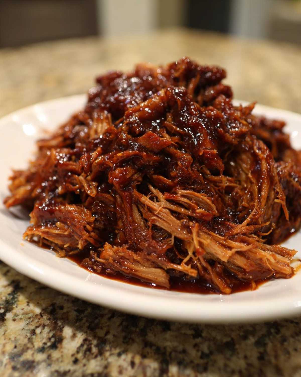 Close-up of tender, shredded slow cooker pulled pork coated in rich, dark BBQ sauce on a white plate.