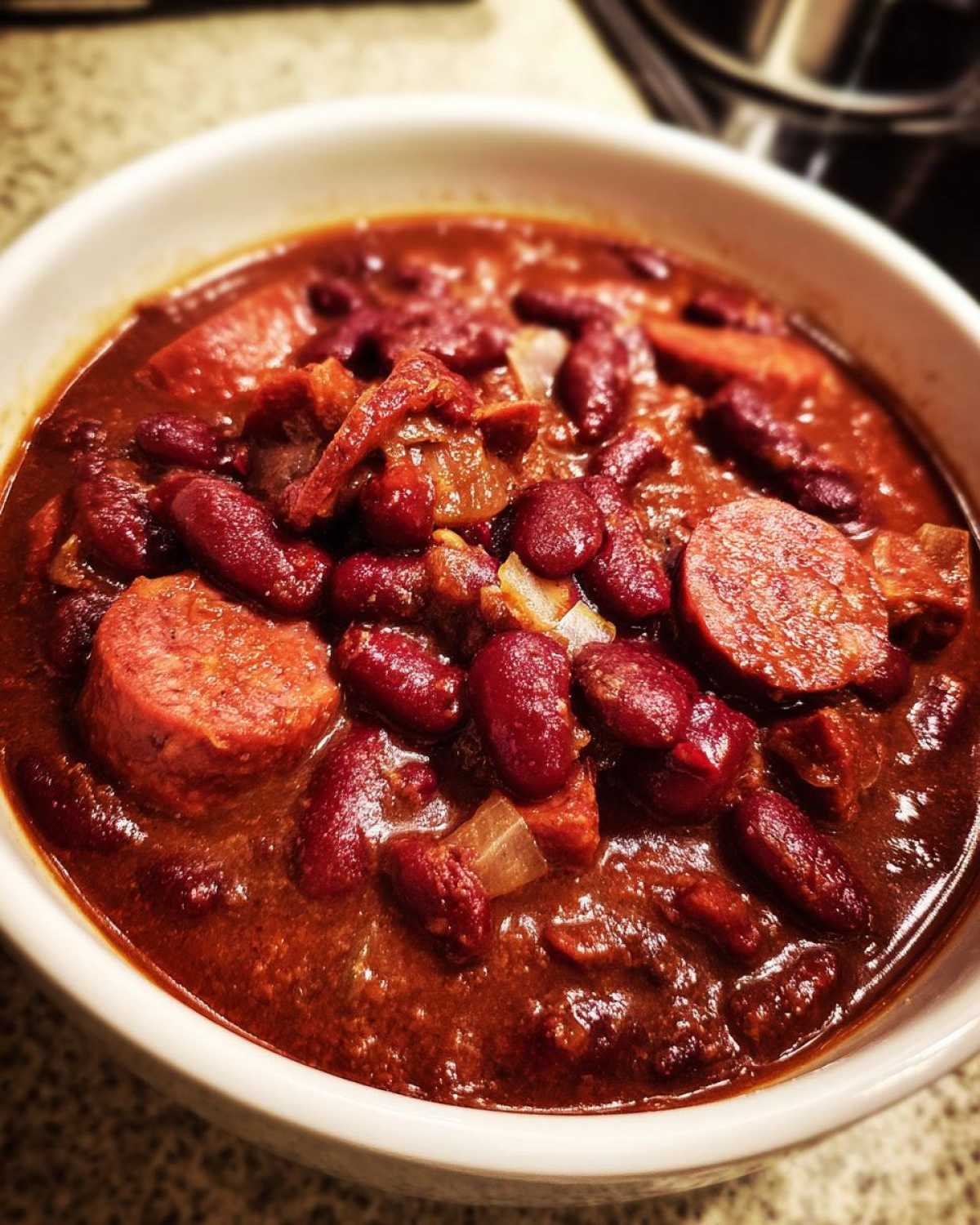 Close-up of a white bowl filled with rich, dark red slow cooker red beans and rice, featuring slices of sausage and onions.