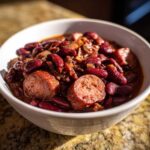 A white bowl filled with rich, saucy slow cooker red beans and rice mixed with slices of smoked sausage.