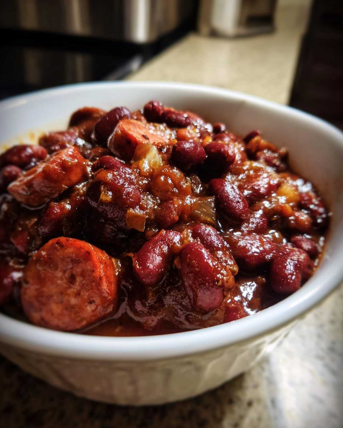 Close-up of a white bowl filled with rich, saucy slow cooker red beans and rice mixed with sliced smoked sausage.