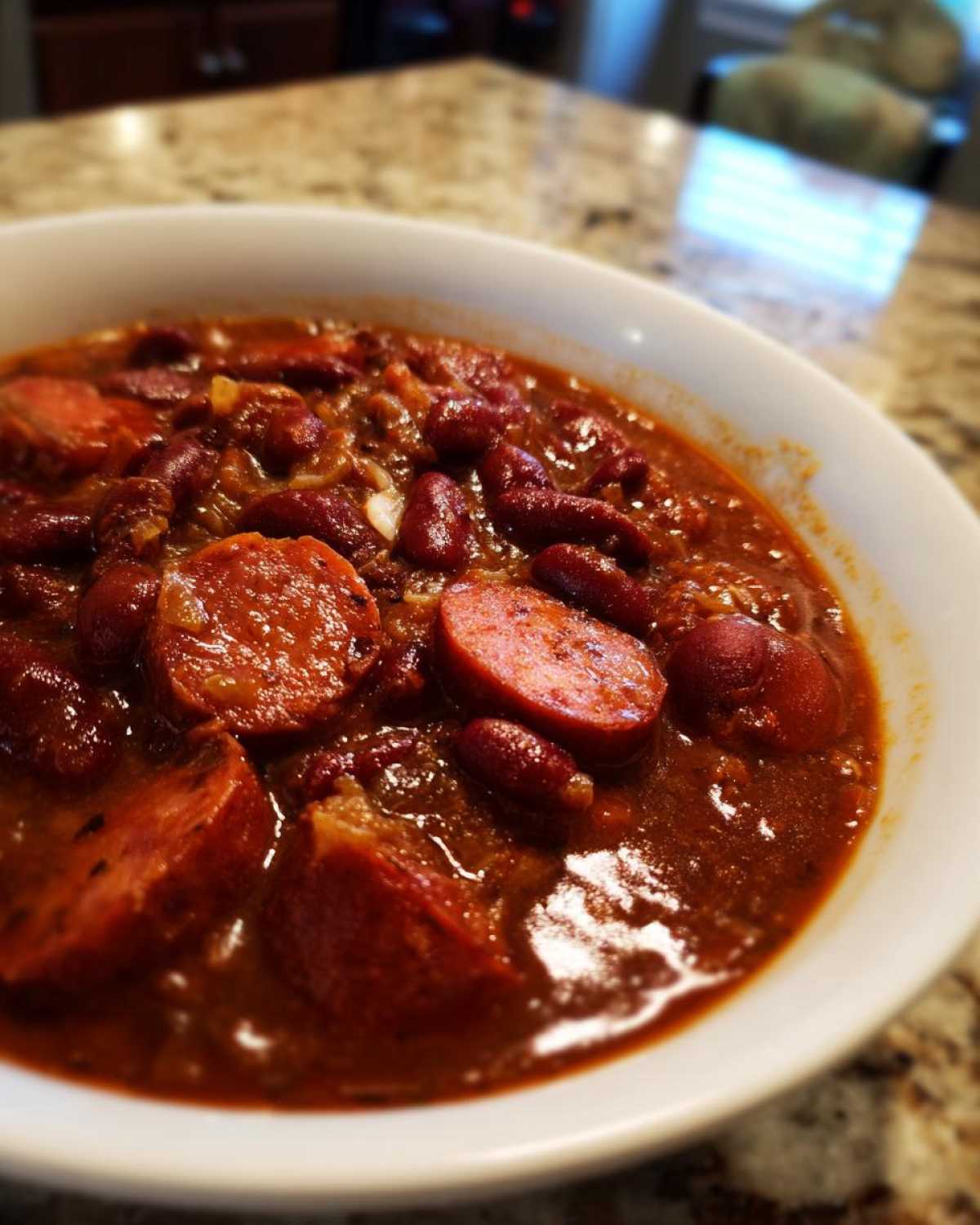 Close-up of a white bowl filled with rich, dark red slow cooker red beans and rice mixed with slices of andouille sausage.