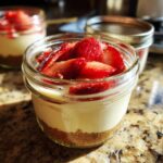 Close-up of a single serving Protein Cheesecake layered in a small glass jar, topped with fresh sliced strawberries.