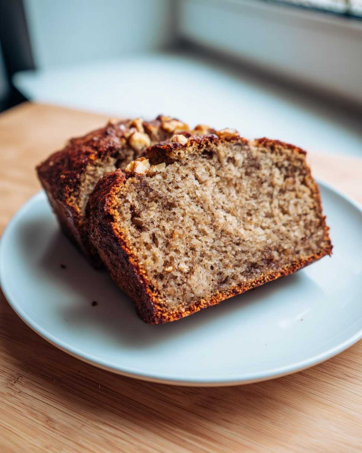 Two slices of moist sugar free banana bread topped with walnuts, served on a light blue plate.