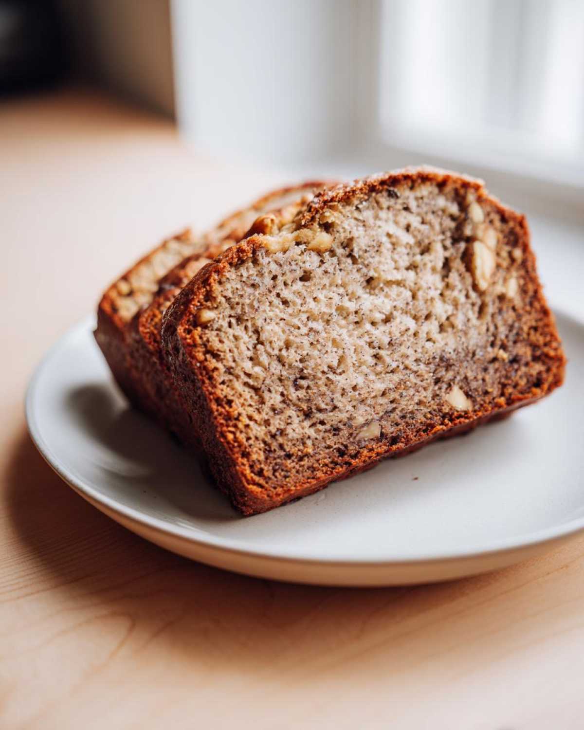 Two thick slices of moist sugar free banana bread with visible walnuts, resting on a light plate.