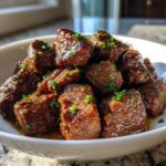 Close-up of tender, saucy crockpot steak bites garnished with fresh parsley in a white bowl.