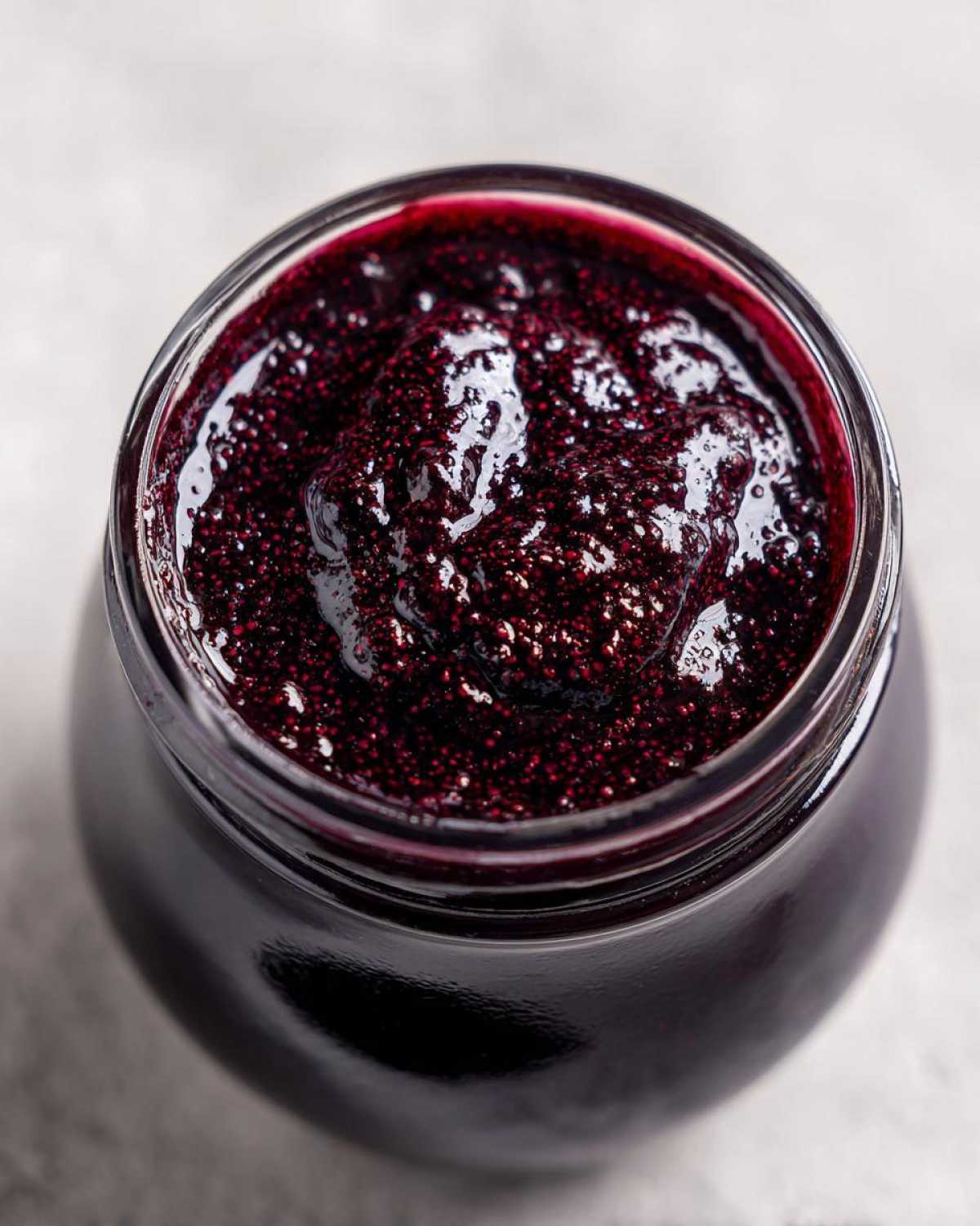 Close-up overhead shot of thick, dark purple elderberry syrup recipe inside a clear glass jar.