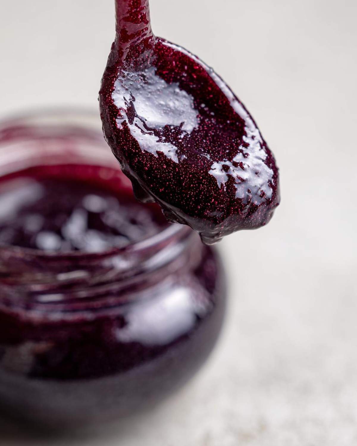 Close-up of thick, dark purple elderberry syrup recipe dripping from a spoon over an open jar.