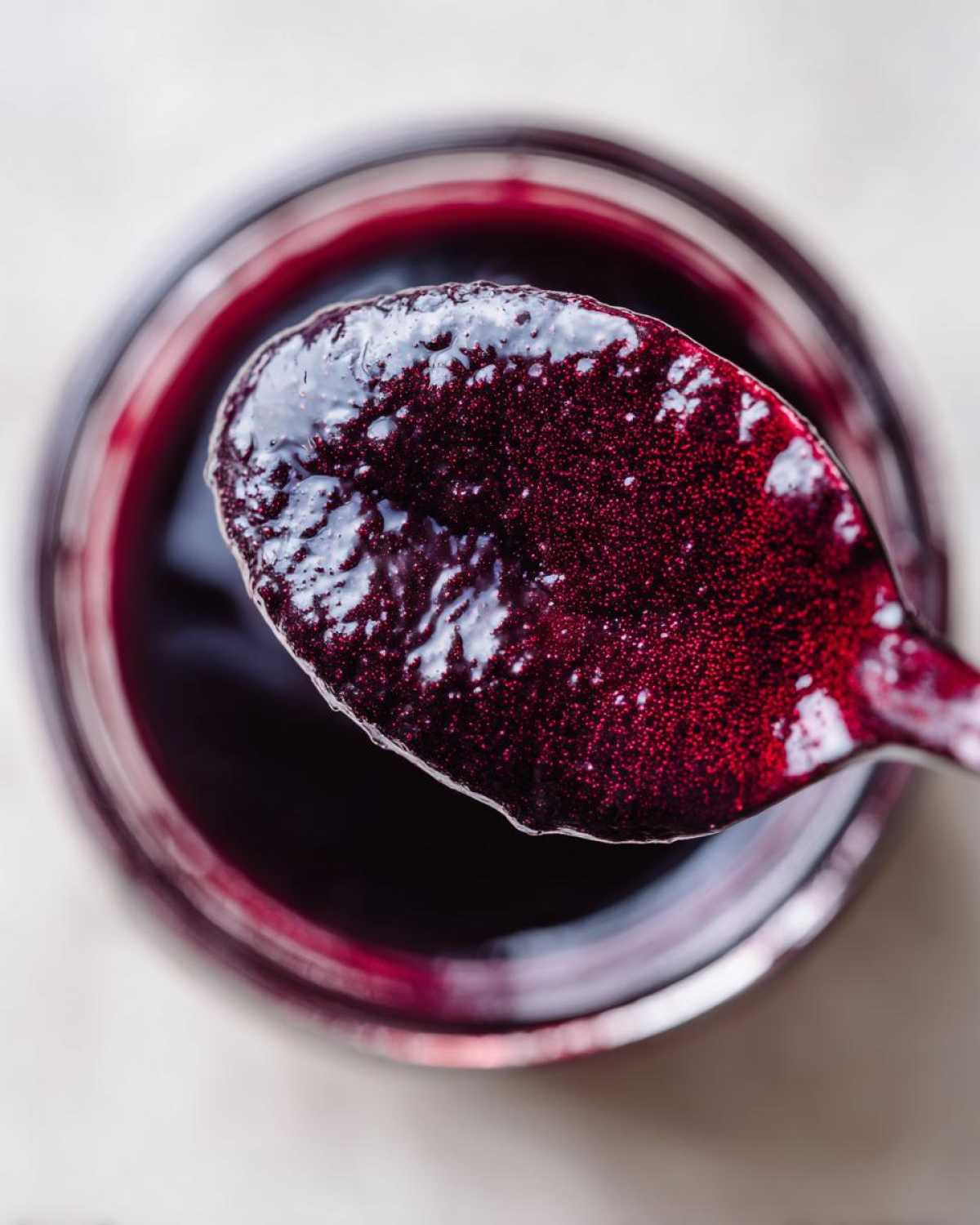 Close-up overhead view of thick, dark purple elderberry syrup recipe being scooped out of a jar on a spoon.