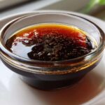Close-up of thick, glossy homemade teriyaki sauce with small bubbles in a clear dipping bowl.