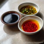 Three small bowls showing ingredients for Dumpling Sauce: dark soy sauce, chili oil, and a scallion/ginger mixture.