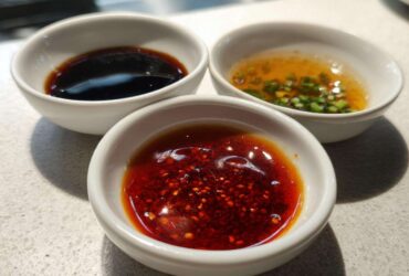 Three small white bowls containing different Dumpling Sauce recipes: chili oil, soy sauce, and a scallion vinaigrette.