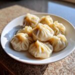A plate piled high with perfectly pleated, steamed Traditional Chinese Dumplings, glistening in natural light.