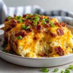 Close-up of a single serving of twice baked potato, loaded with melted cheddar cheese, bacon bits, and green onions.