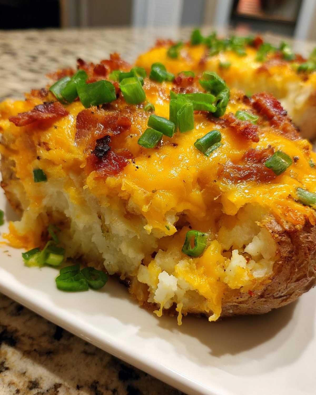 A close-up view of a twice baked potato half, loaded with melted cheddar cheese, bacon bits, and fresh green onions.