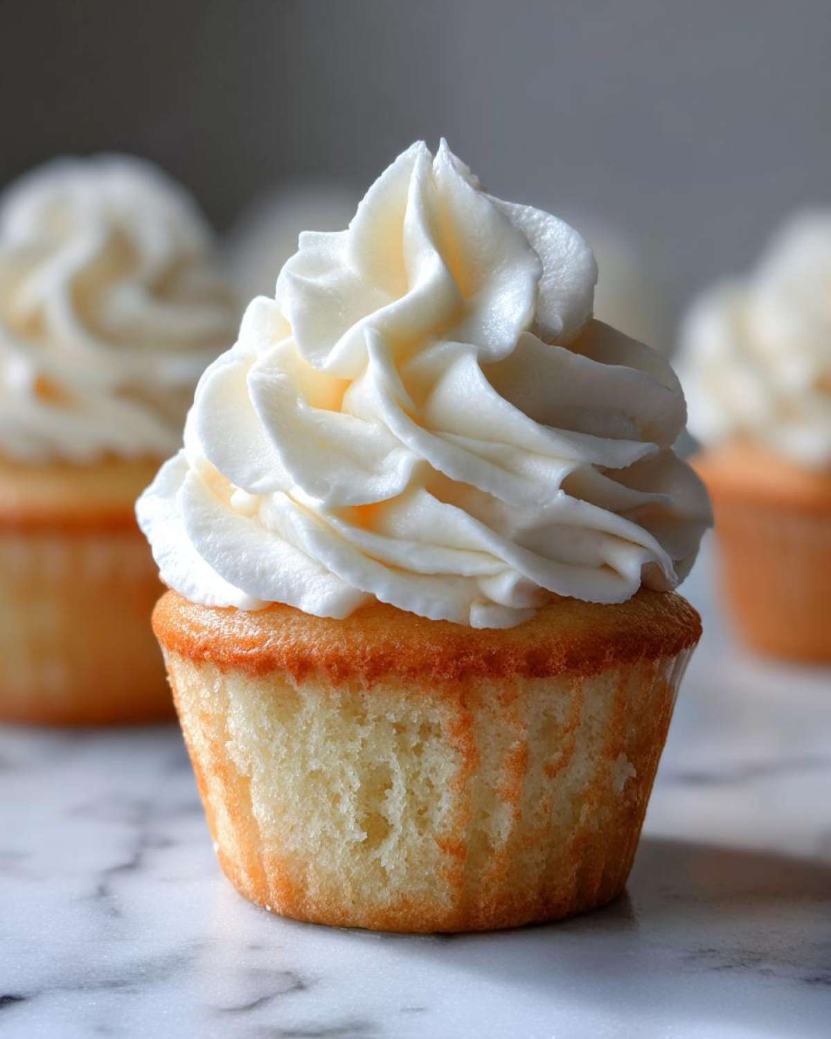 Close-up of a single, moist vanilla cupcake topped with a generous swirl of white vanilla buttercream frosting.