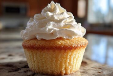 A single, perfectly baked vanilla cupcake topped with a generous swirl of white frosting.