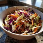 Close-up of a vibrant cabbage salad with shredded purple and green cabbage and carrots in a white bowl.