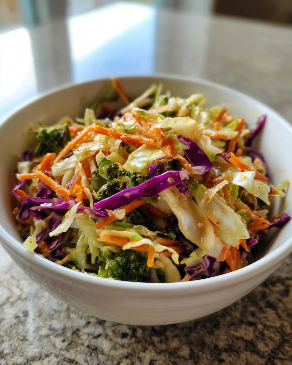 Close-up of a vibrant cabbage salad mix featuring shredded white and purple cabbage, carrots, and broccoli florets.