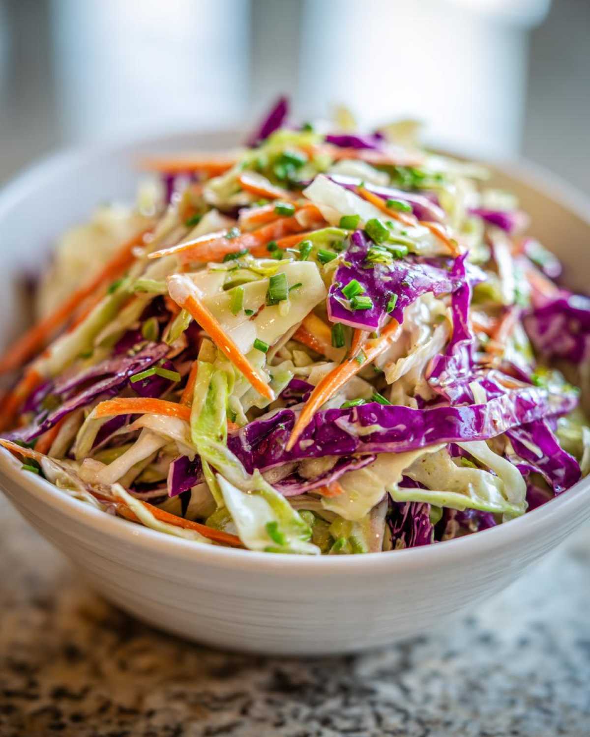 Close-up of vibrant cabbage salad featuring shredded green and purple cabbage, carrots, and chives in a white bowl.