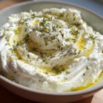 A close-up view of a bowl filled with fluffy, creamy whipped feta dip, drizzled with olive oil and sprinkled with dried herbs.