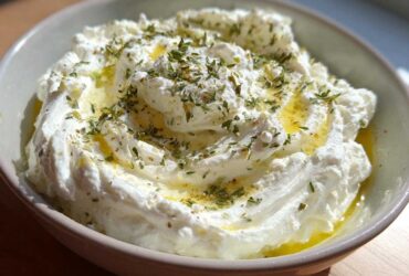A close-up view of a bowl filled with fluffy, creamy whipped feta dip, drizzled with olive oil and sprinkled with dried herbs.