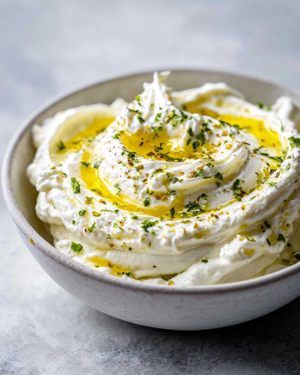 Close-up of a bowl filled with fluffy whipped feta dip, drizzled with olive oil and sprinkled with herbs.