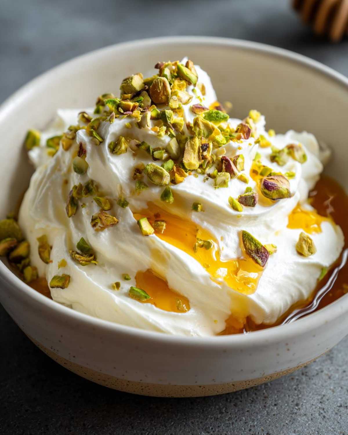 Close-up of creamy whipped goat cheese drizzled with honey and topped with chopped green pistachios.