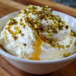 A white bowl filled with fluffy whipped goat cheese topped with chopped pistachios and a drizzle of golden honey.