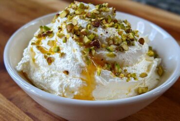 A white bowl filled with fluffy whipped goat cheese topped with chopped pistachios and a drizzle of golden honey.