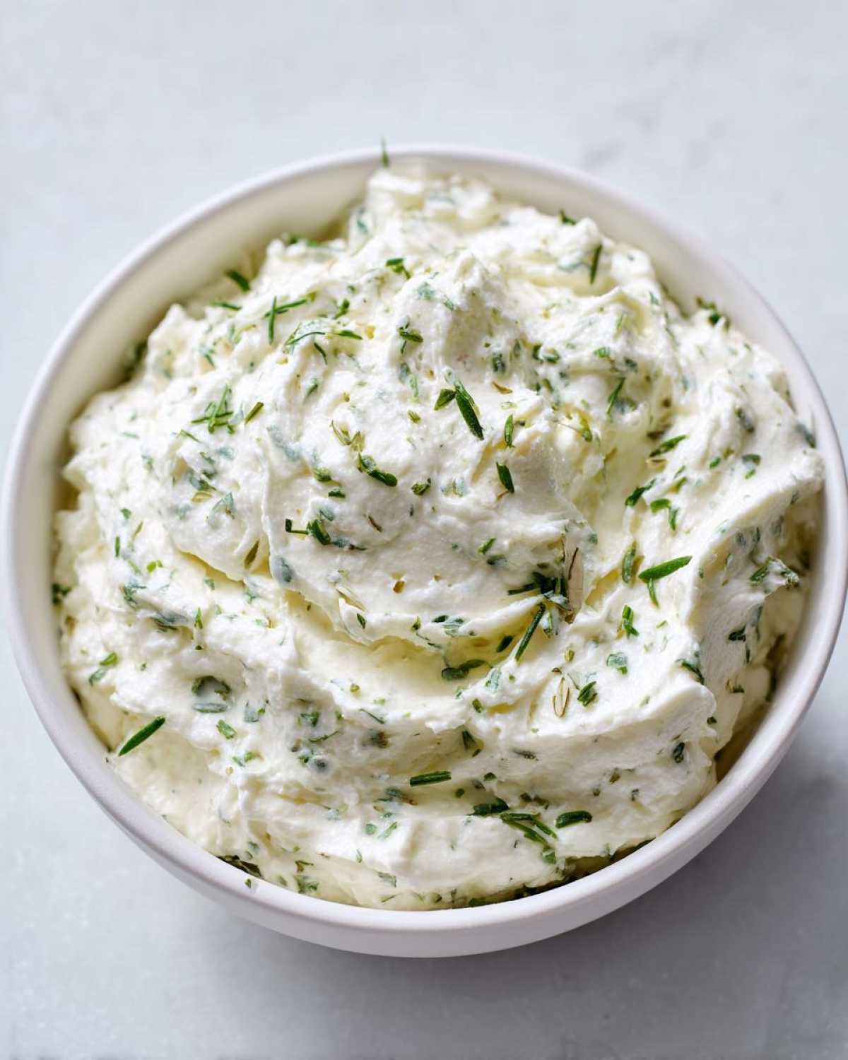 Close-up of thick, creamy 5-Minute Greek Yogurt Ranch Dip topped with fresh green herbs in a white bowl.