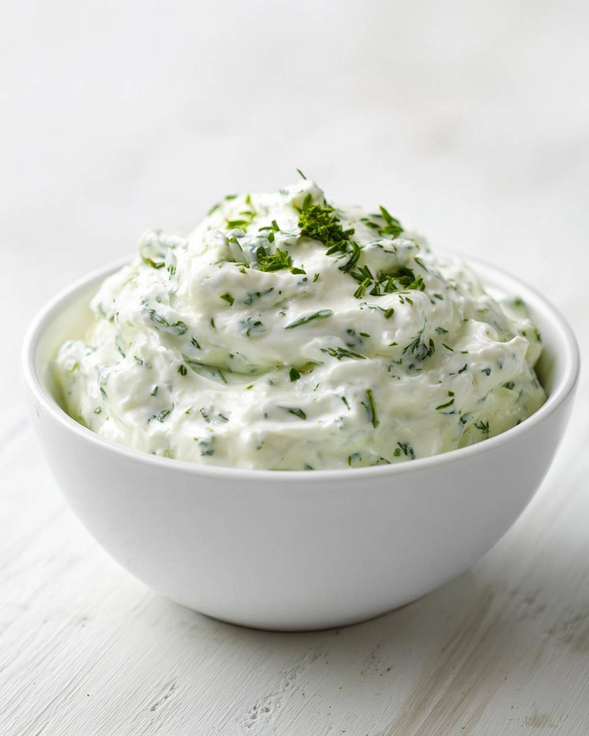 A close-up of thick, creamy 5-Minute Greek Yogurt Ranch Dip speckled with green herbs in a white bowl.