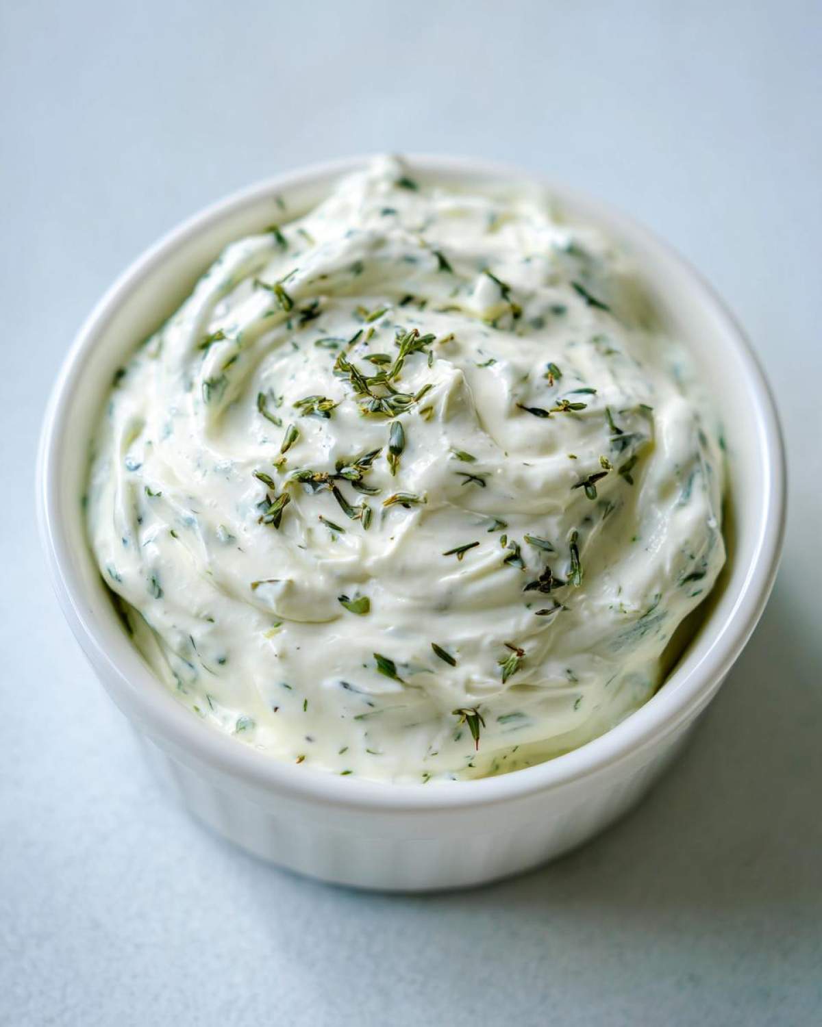 Close-up of creamy 5-Minute Greek Yogurt Ranch Dip garnished with dried herbs in a white ramekin.
