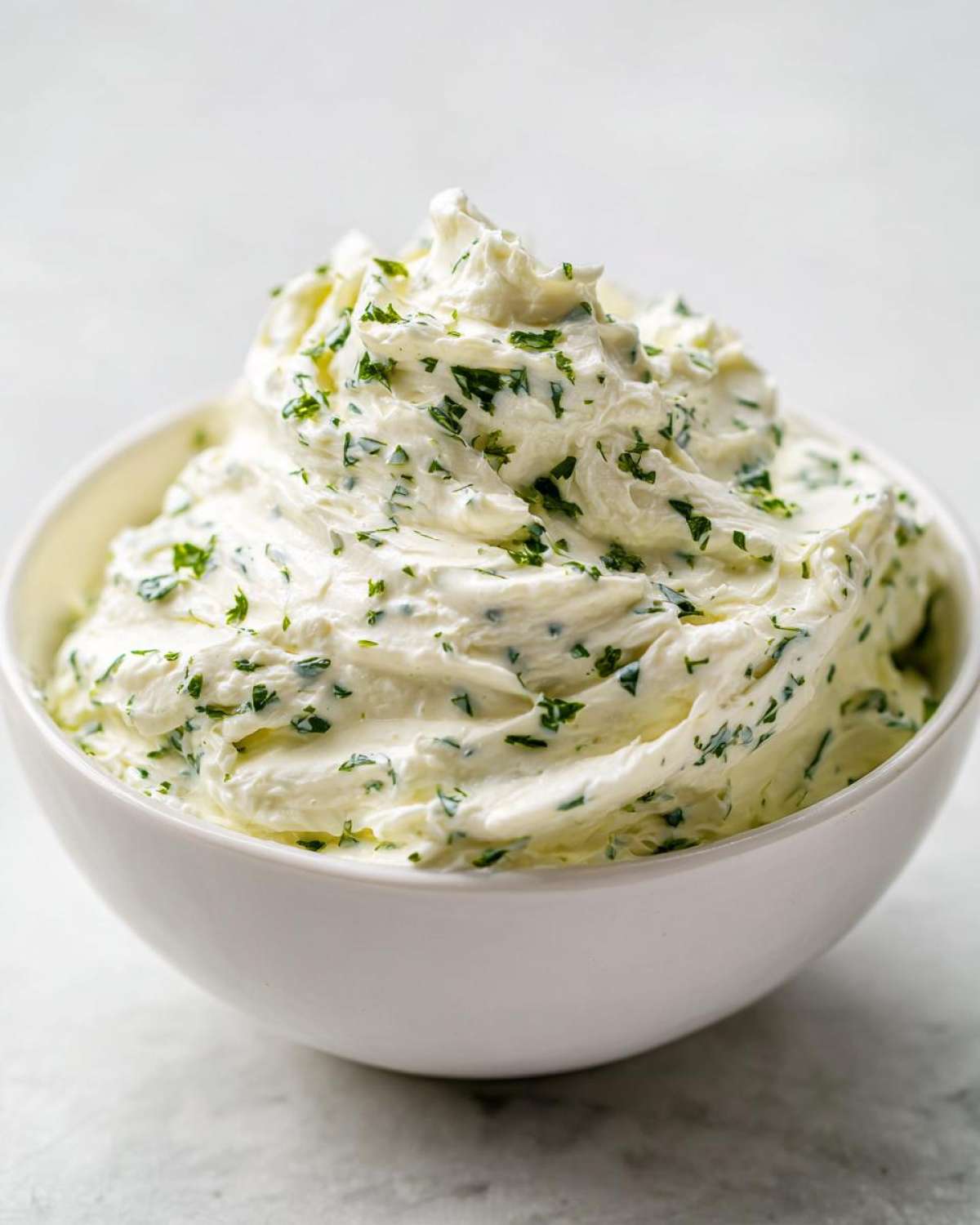 A close-up of thick, creamy 5-Minute Greek Yogurt Ranch Dip topped with fresh green herbs in a white bowl.