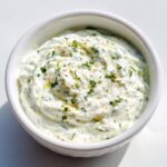 A close-up overhead shot of thick 5-Minute Greek Yogurt Ranch Dip garnished with fresh herbs in a white bowl.