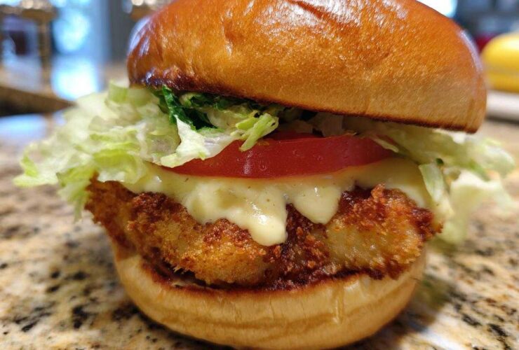 Close-up of a golden, crispy Air Fryer Crispy Fish Sandwich topped with melted sauce, tomato, and lettuce.