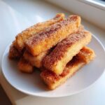 A stack of golden brown Air Fryer French Toast Sticks generously coated in cinnamon sugar on a white plate.